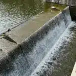 Wasser strömt über die Krone eines Wehrs an einem Fluss