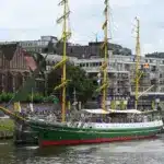 Grüner Dreimaster mit gelben Masten vor der historischen Bremer Uferbebauung