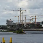 Zahlreiche Baukräne über einer Großbaustelle hinter einer Eisenbahnbrücke über die Weser