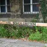 Handbeschriftetes Holzschild Schulgarten vor einem bewachsenen Beet an einer Schulwand