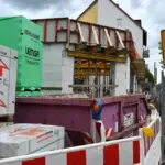 Rohbau mit gestapeltem Baumaterial und Container hinter einer Absperrung