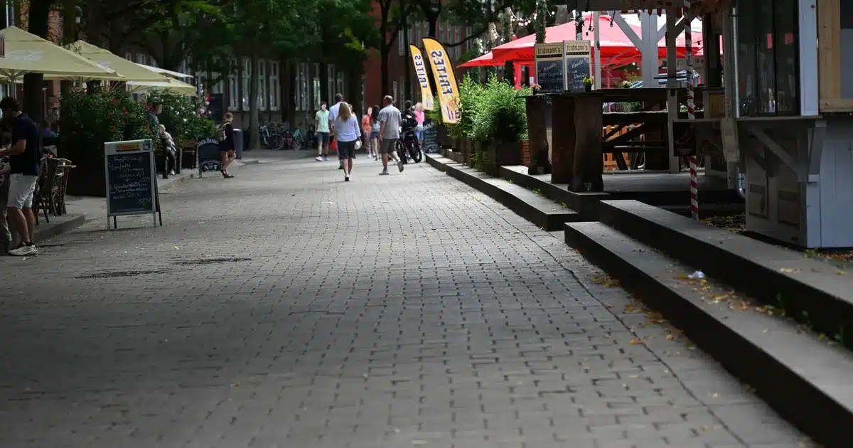 Gepflasterte Straße mit Imbissbude, Außengastronomie und Passanten