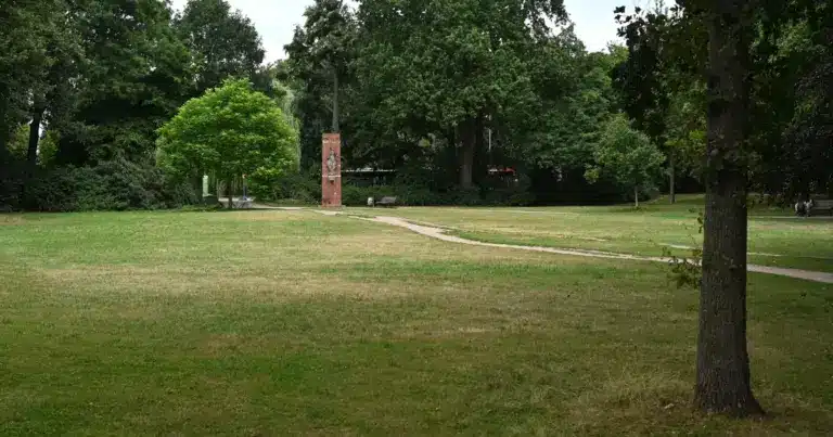 Weite Rasenfläche in einer Parkanlage mit Wegen und einem Backsteindenkmal